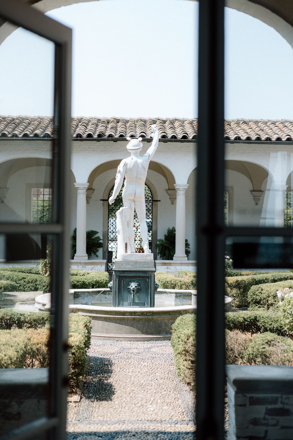View through window bars of a Mediterranean courtyard with white arches and classical statues.