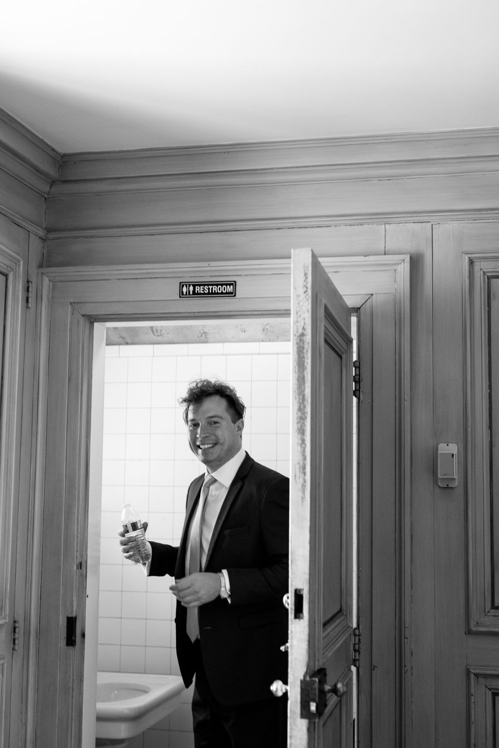 A black and white photo sequence shows someone in a suit walking past a restroom door in a hallway.