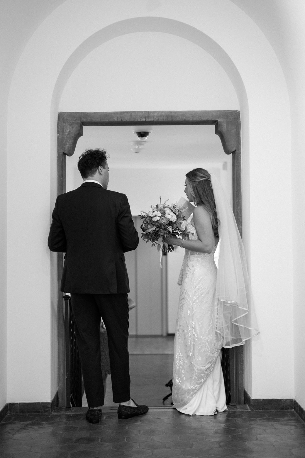 Black and white wedding photos showing a couple walking through an arched hallway.