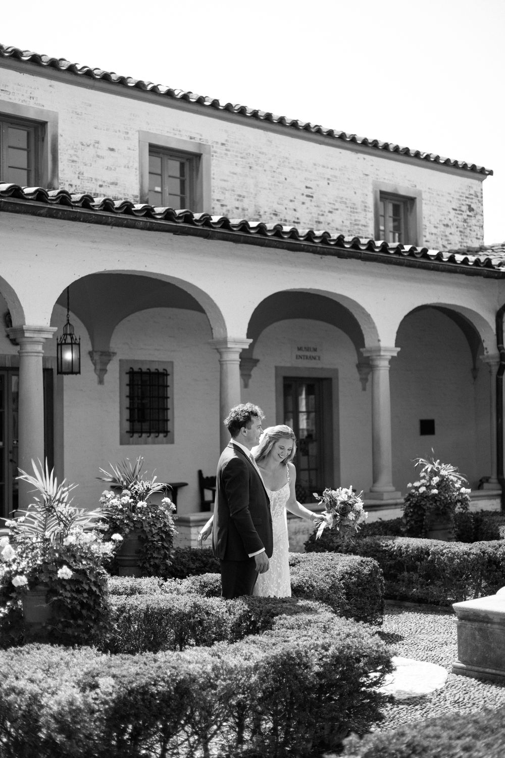A Mediterranean-style building with white stucco walls and arched colonnade features beautiful landscaping.