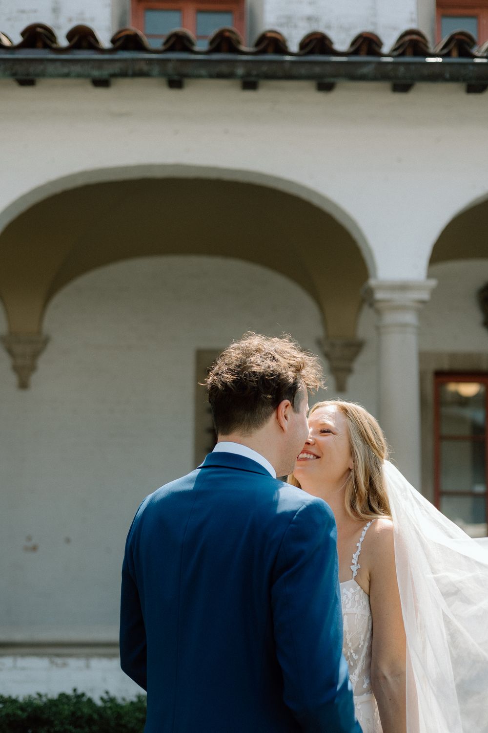 Wedding couple shares intimate moment under Mediterranean-style arches with terracotta roof tiles.