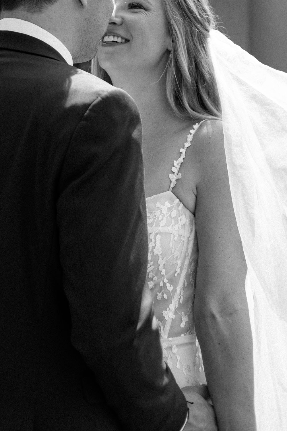 Black and white close-up of a bride in a lace wedding dress with flowing veil.