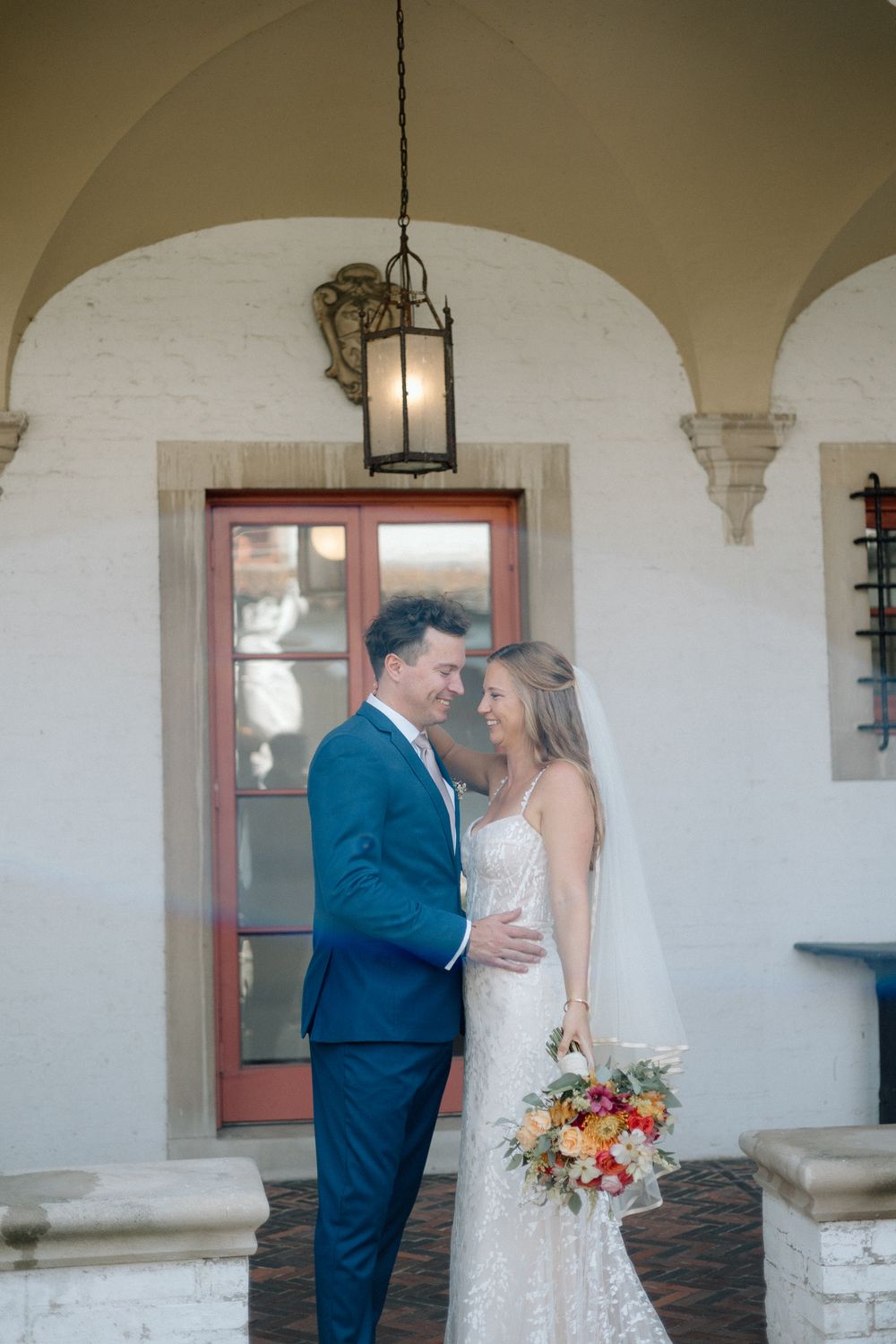Romantic wedding portrait under an arched walkway with a bride holding a colorful bouquet.