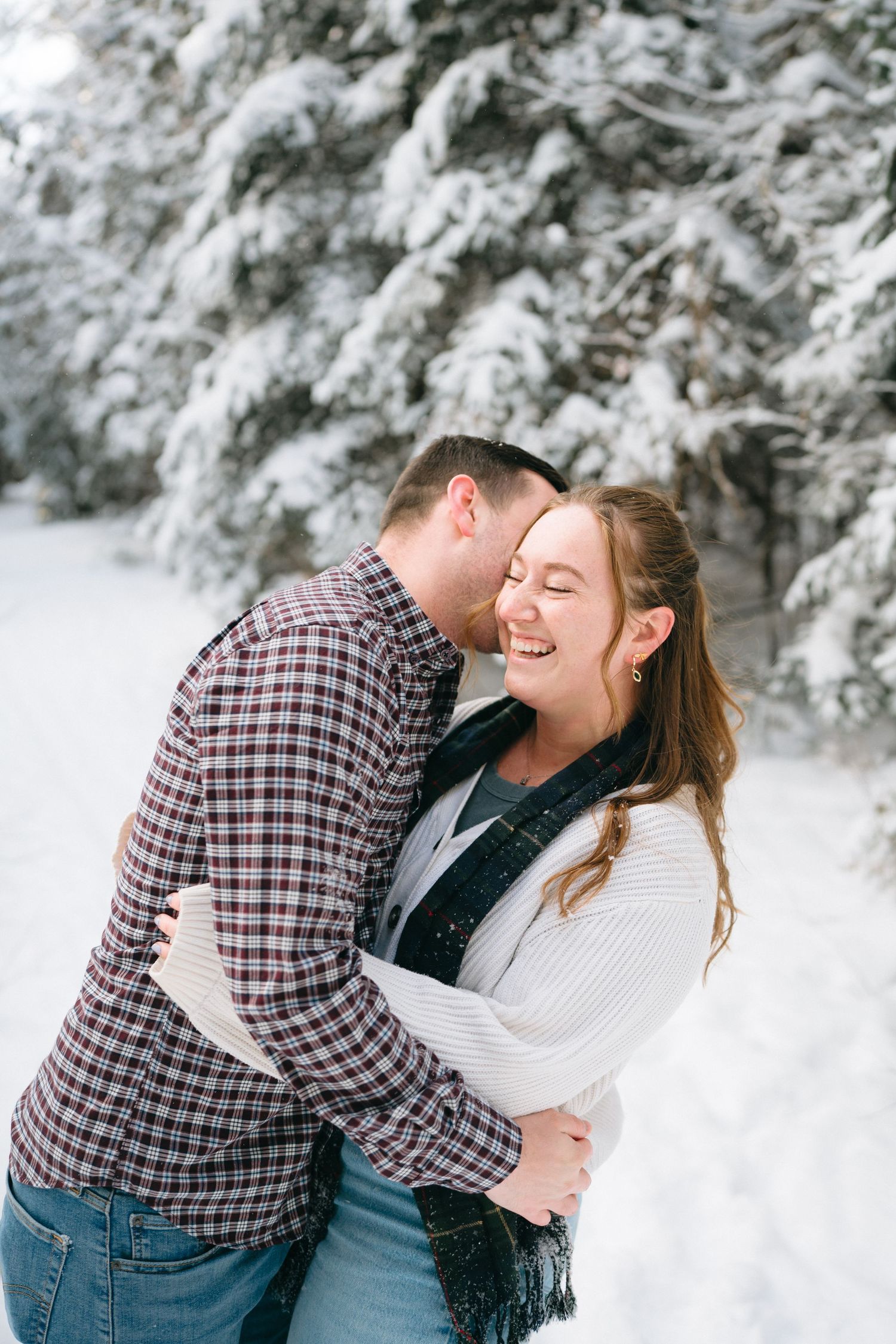 A couple shares joyful moments in a snowy winter landscape wearing cozy sweaters and plaid.