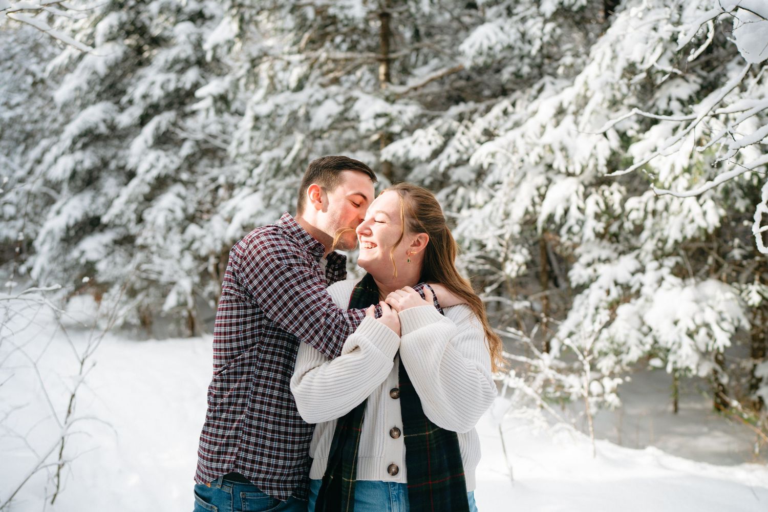 A romantic winter moment between two people sharing laughter in a snow-covered forest setting.