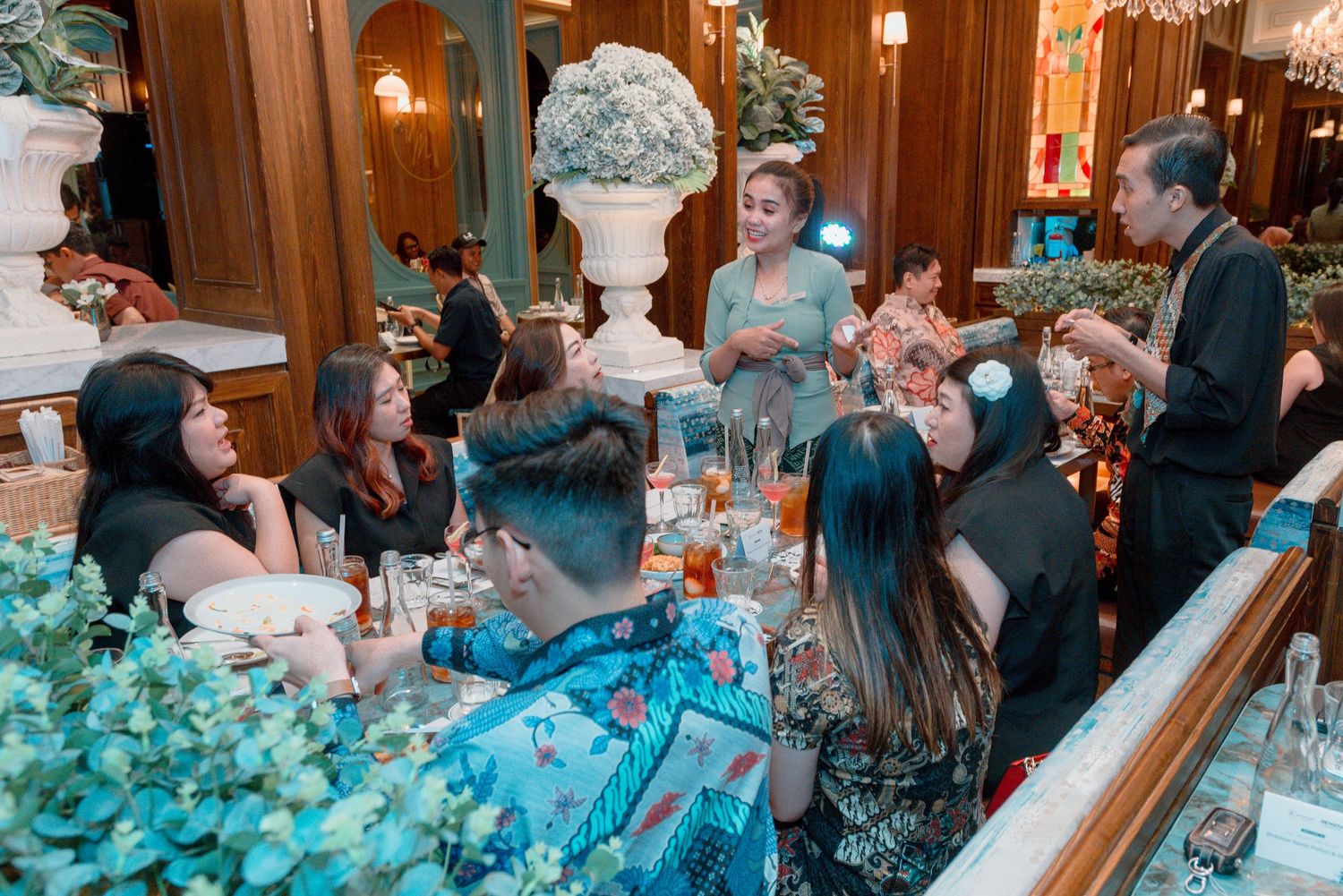 Guests gather around an elegantly decorated table with turquoise decor and floral centerpieces at an upscale dinner event.