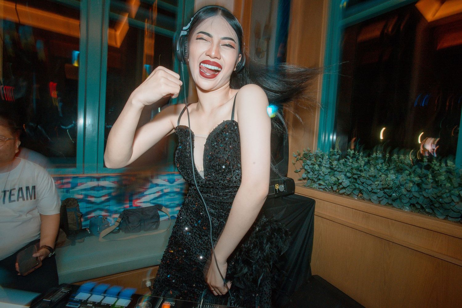 Person in black evening dress laughs joyfully while posing in front of illuminated interior space.