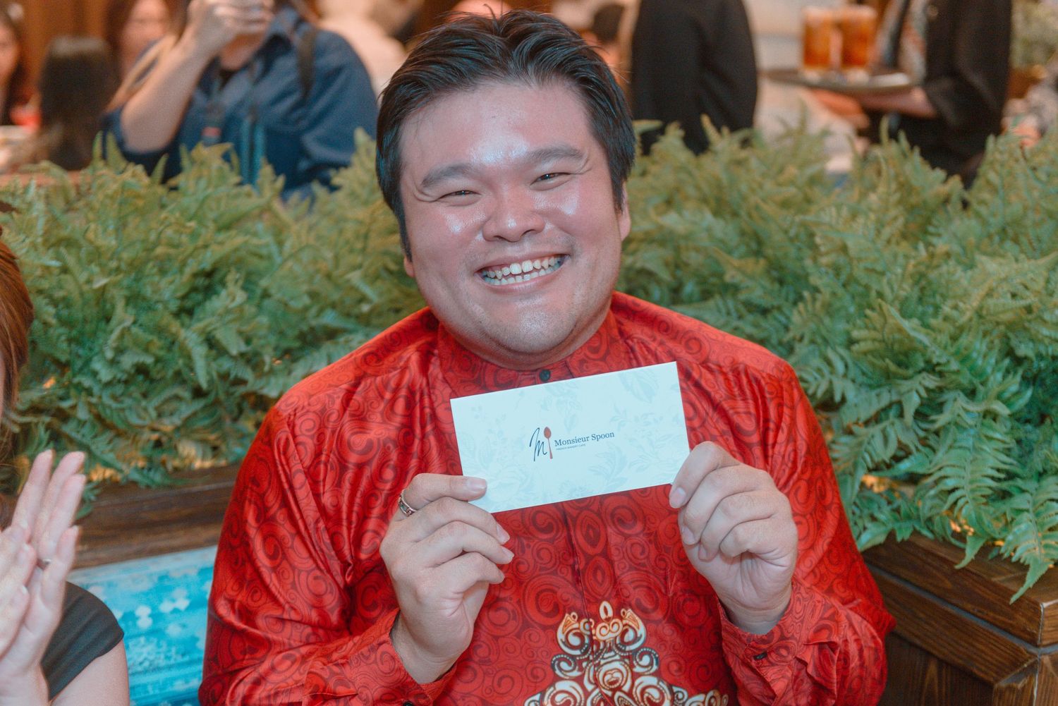 Person in red traditional attire displaying invitation card at formal gathering.