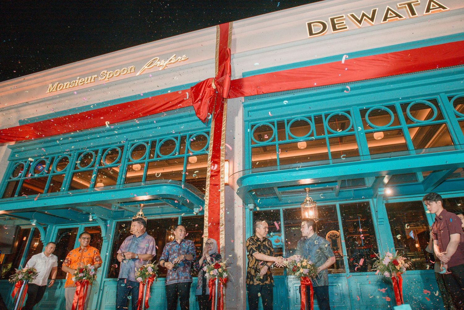 A long row of red and turquoise colored restaurant storefronts with outdoor seating along a street at night.