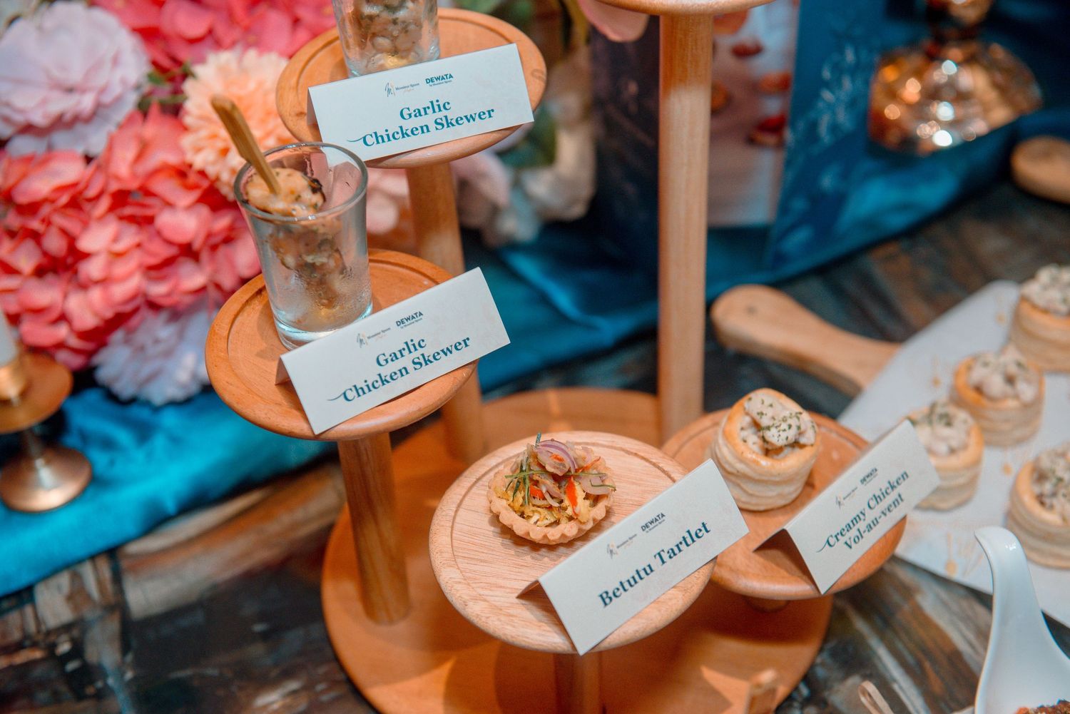 Small desserts and treats displayed on wooden stands with name cards at an elegant event setup.