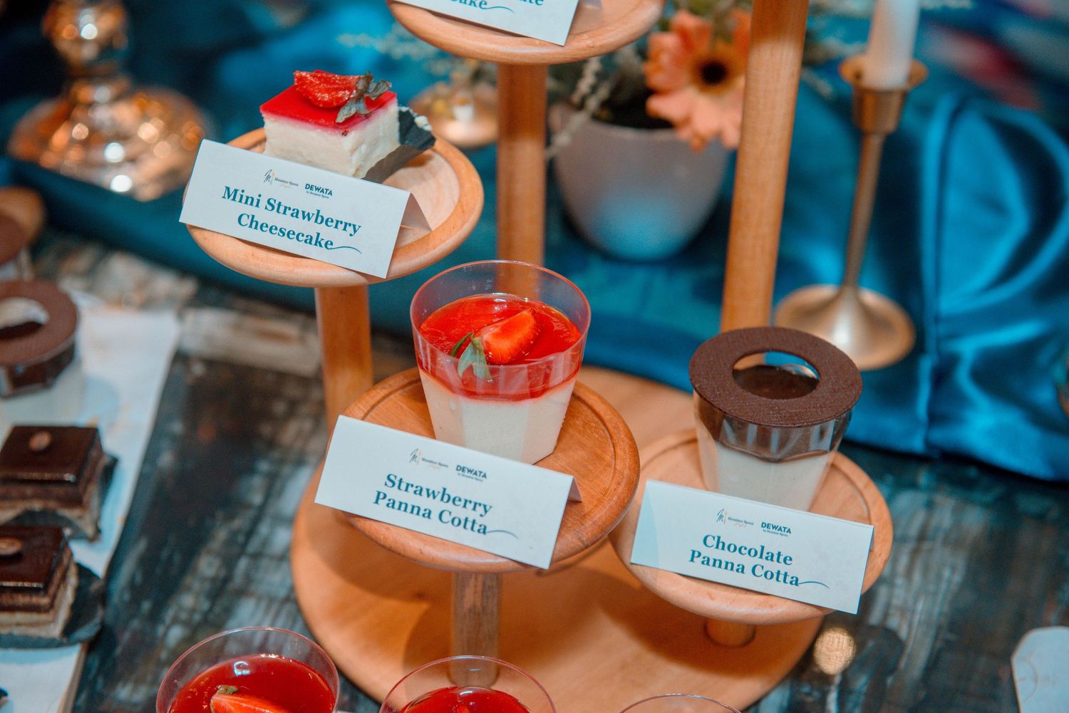 Colorful cupcakes with white frosting and red sprinkles displayed on a dessert table with blue lighting.