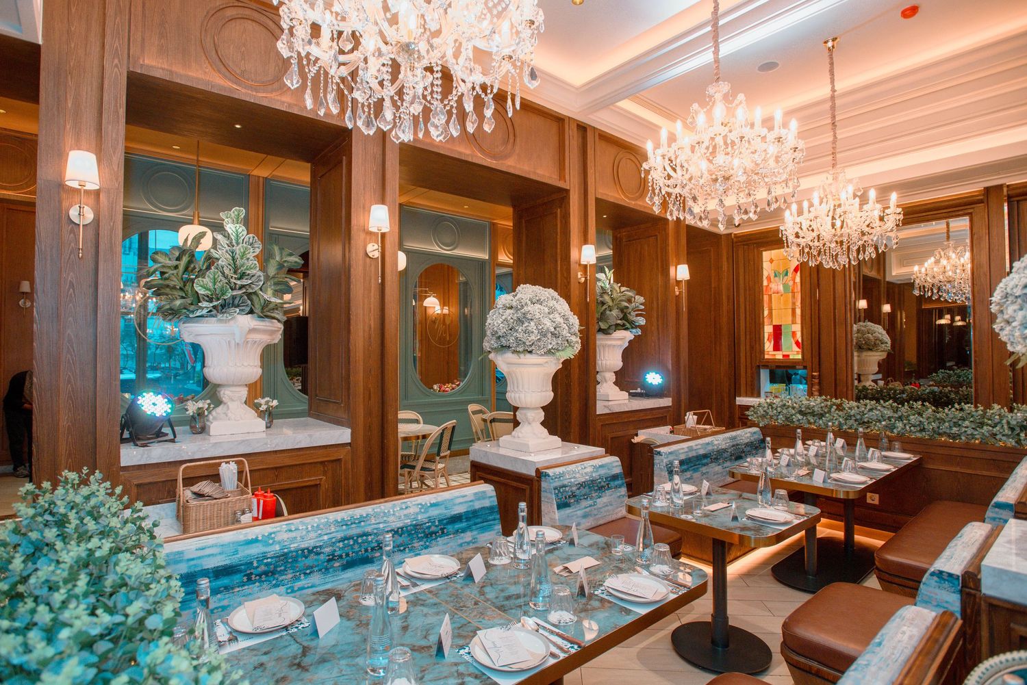 Elegant dining room with crystal chandeliers and wood paneling features luxurious table settings and teal floral arrangements.