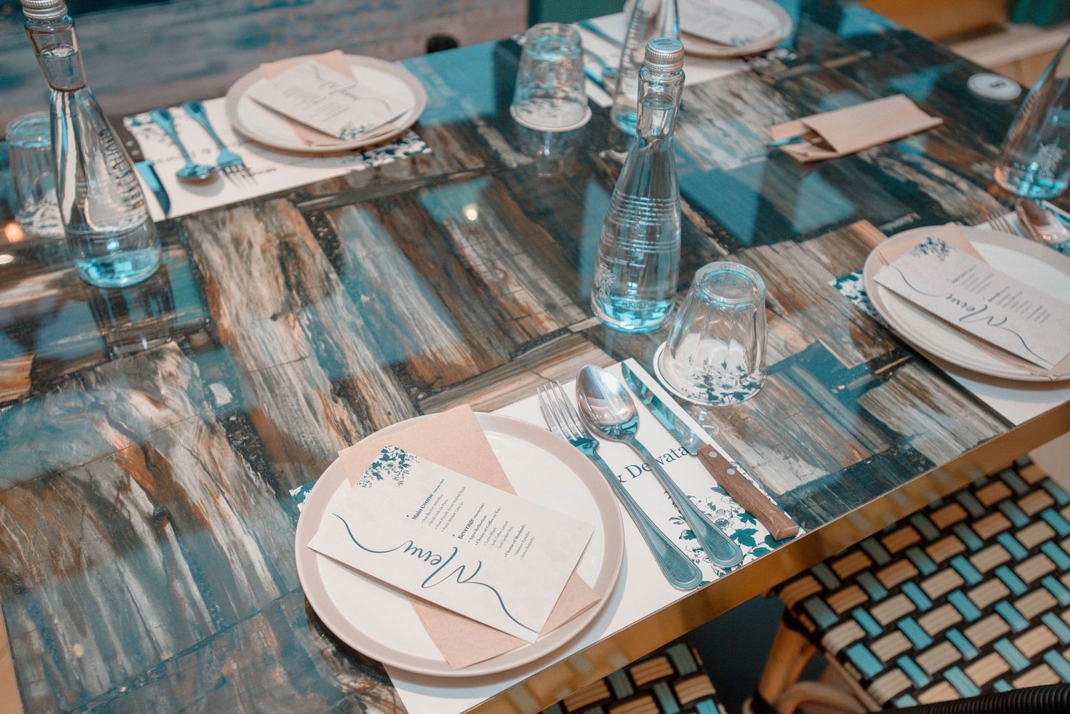 Place settings with white plates and cutlery arranged on a rustic blue wooden table with turquoise water glasses.