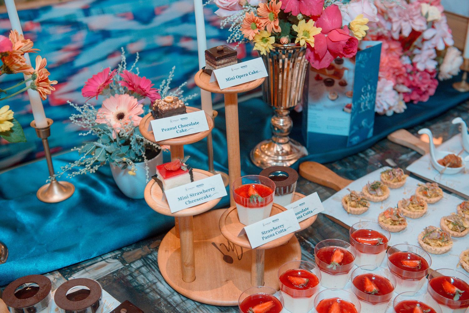 Elegant wedding reception table decorated with teal linens, pink flowers, and golden candle holders displaying appetizers.