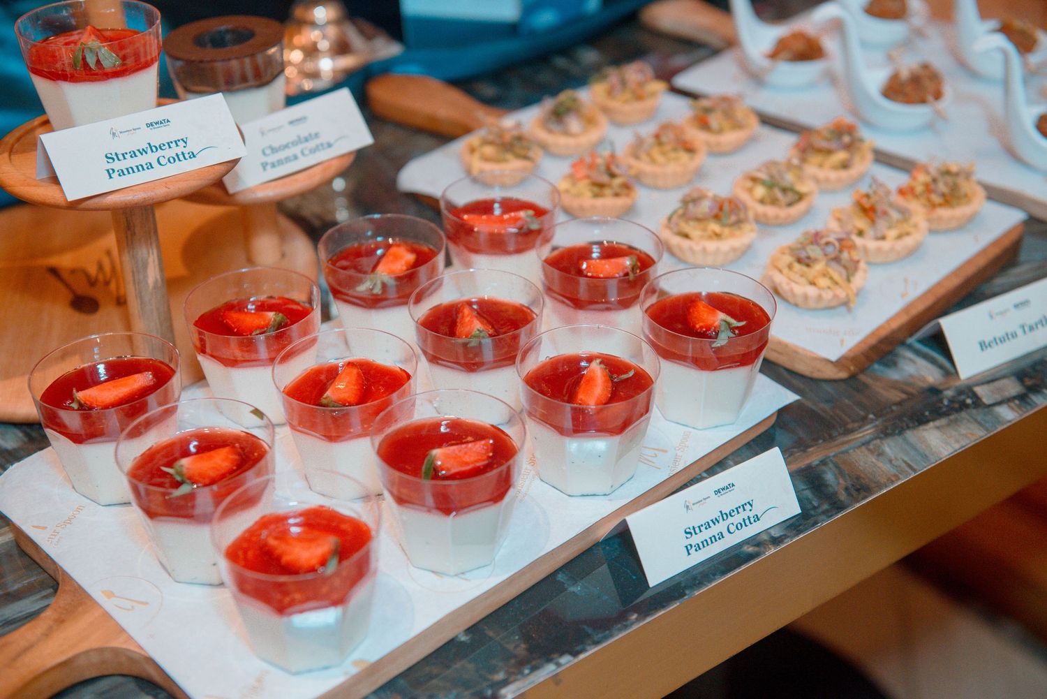 Rows of elegant desserts with bright red toppings displayed on white serving plates at a catering event.