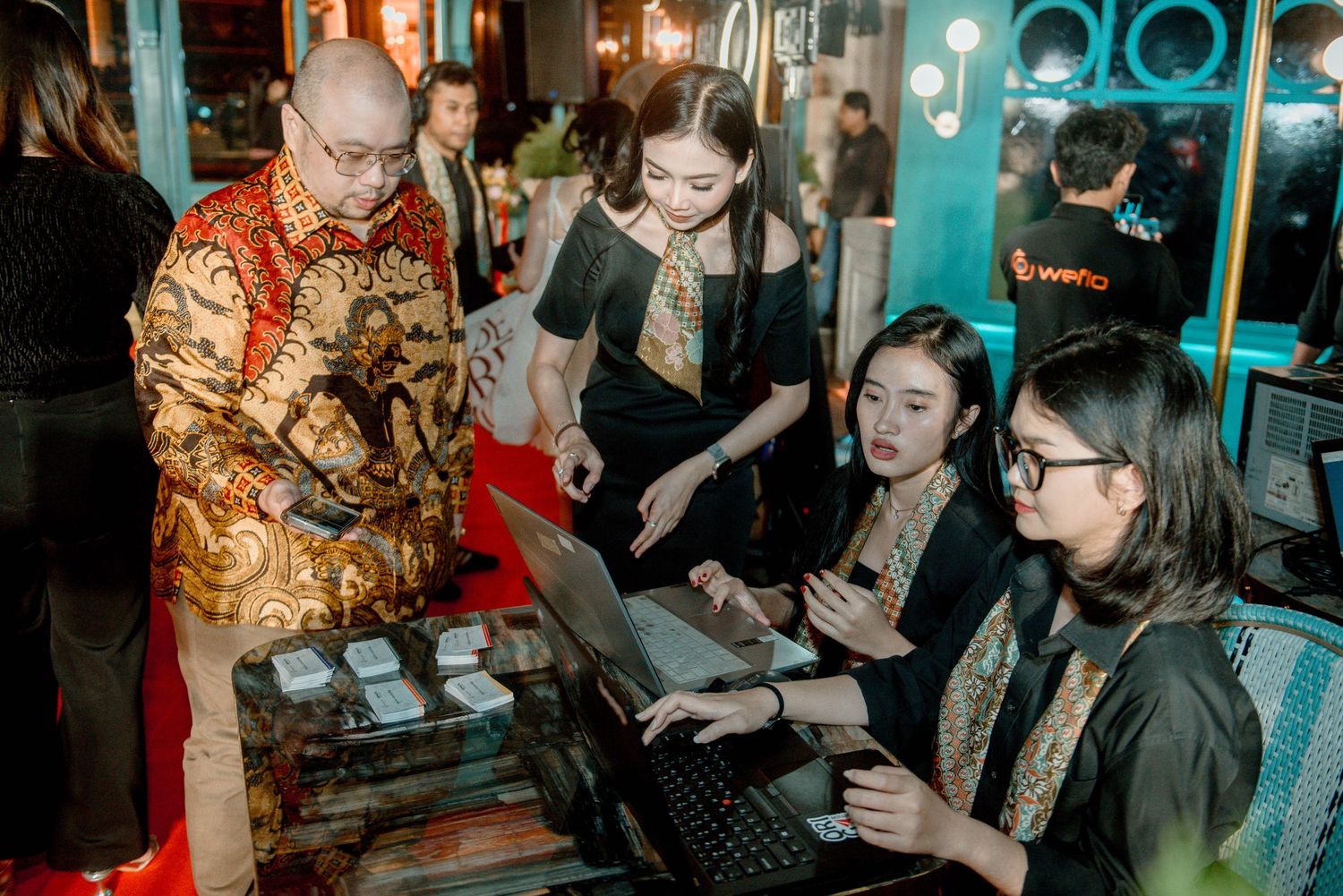 A group gathers around a traditional tea ceremony setup in a dimly lit room with turquoise decor.