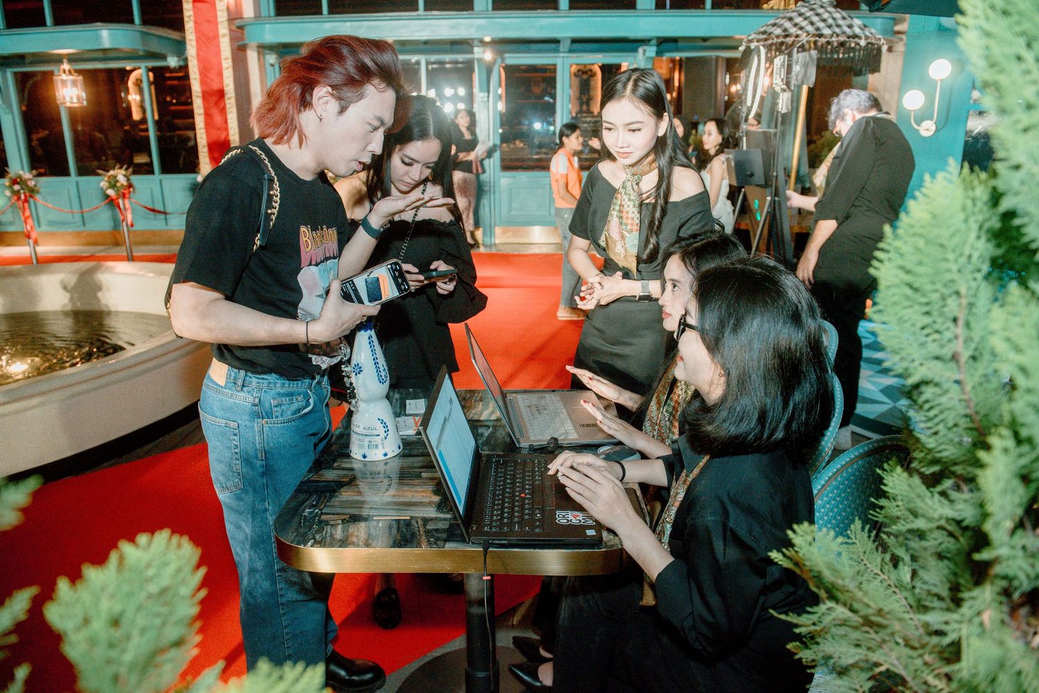 People mingling at an indoor event with teal decor and evergreen trees visible in the background.