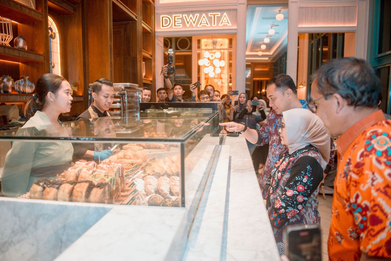 Customers eagerly line up at a bakery counter display case filled with fresh baked goods and pastries.