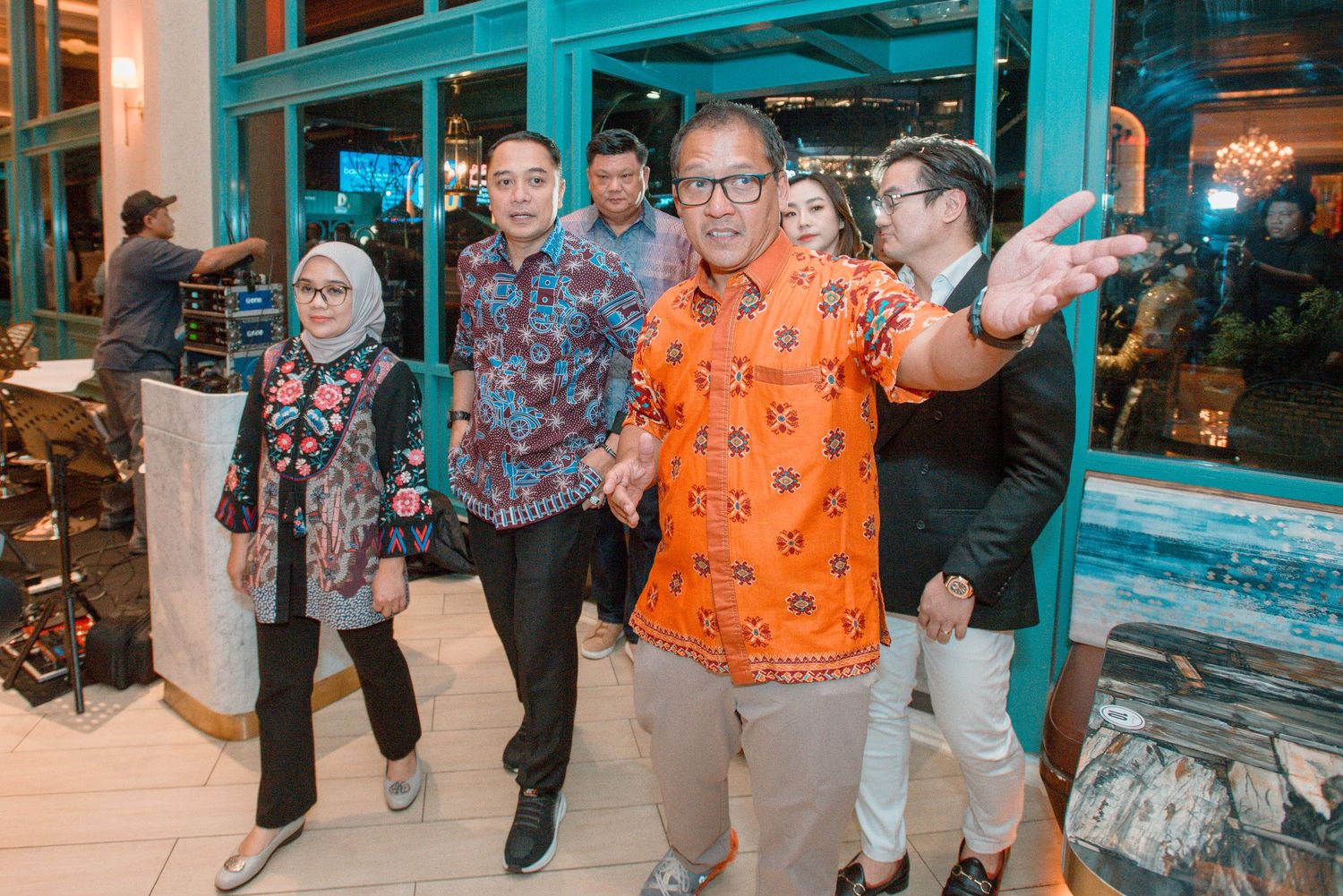 A group of people pose together outside a storefront with blue-tinted windows during an evening gathering.