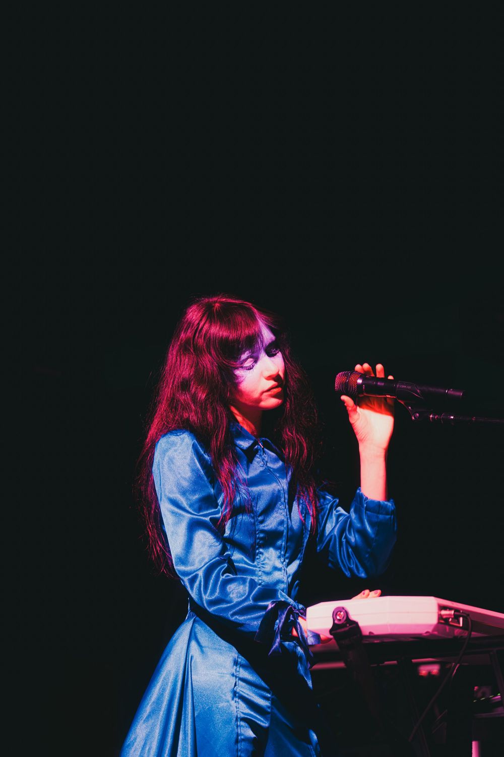 A performer in a blue dress sings on stage under dramatic red lighting during a concert performance.