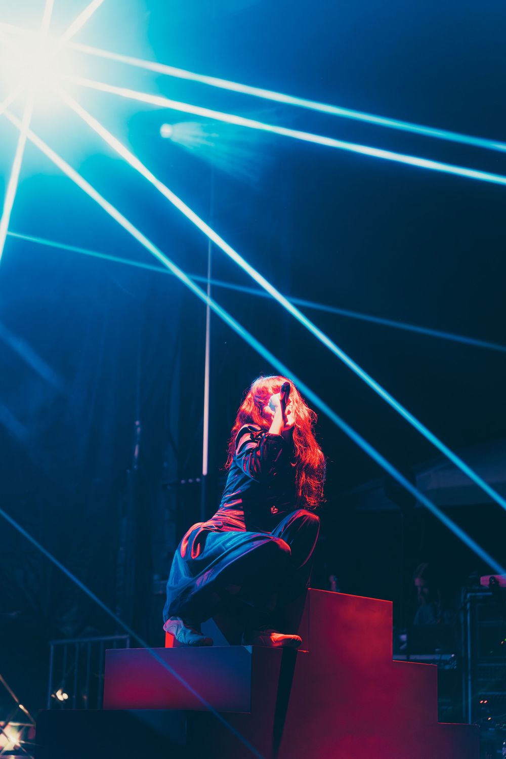 Concert performer silhouetted against dramatic blue stage lighting with bright white beams creating dynamic atmosphere.