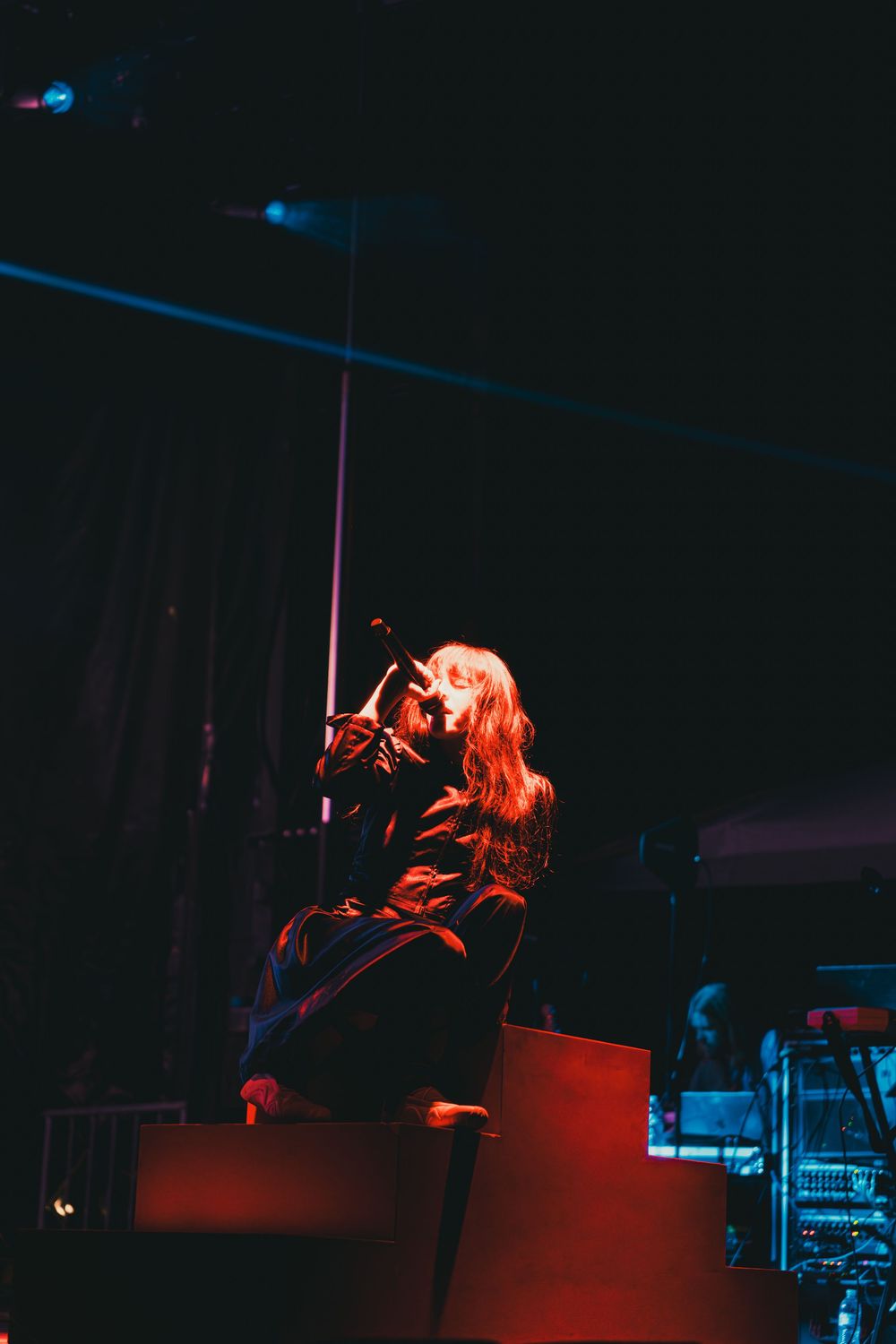 A performer sings passionately on stage bathed in dramatic red and blue lighting during a concert performance.