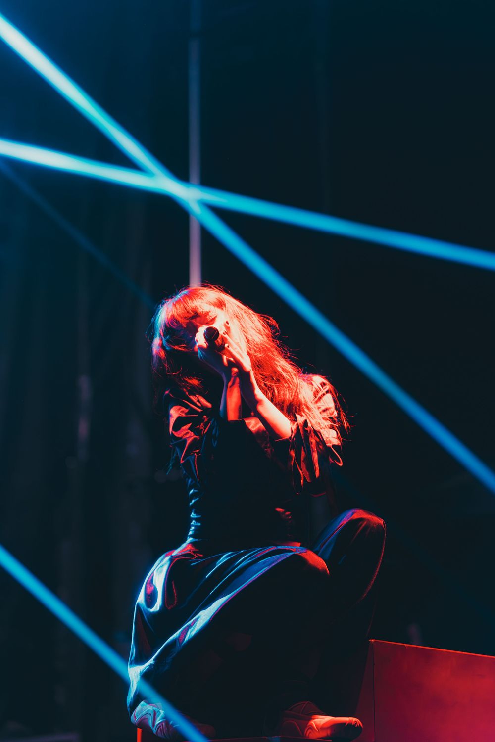 Concert performer with red hair illuminated by dramatic blue stage lighting during an energetic musical performance.