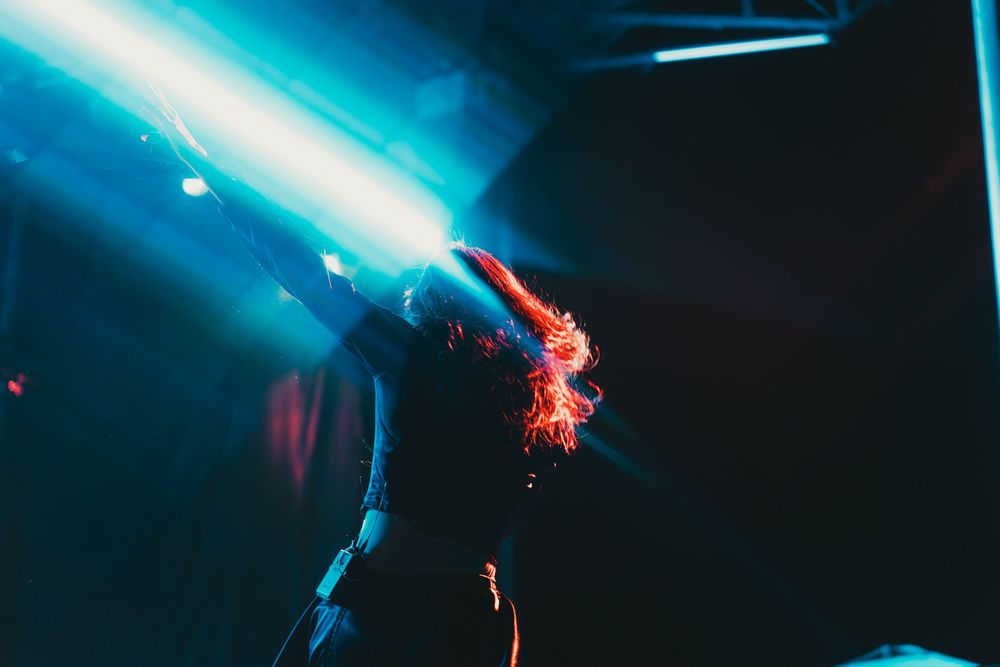 Dramatic blue stage lighting illuminates a dark performance space with red accent lights glowing in the background.