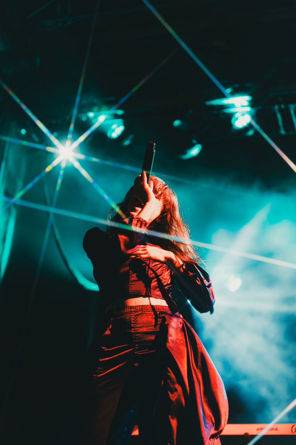 Concert performer silhouetted in dramatic red and blue lighting on stage during an energetic live performance.