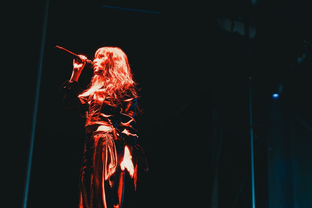 A silhouetted performer in flowing dress sings on a dimly lit stage bathed in red lighting.