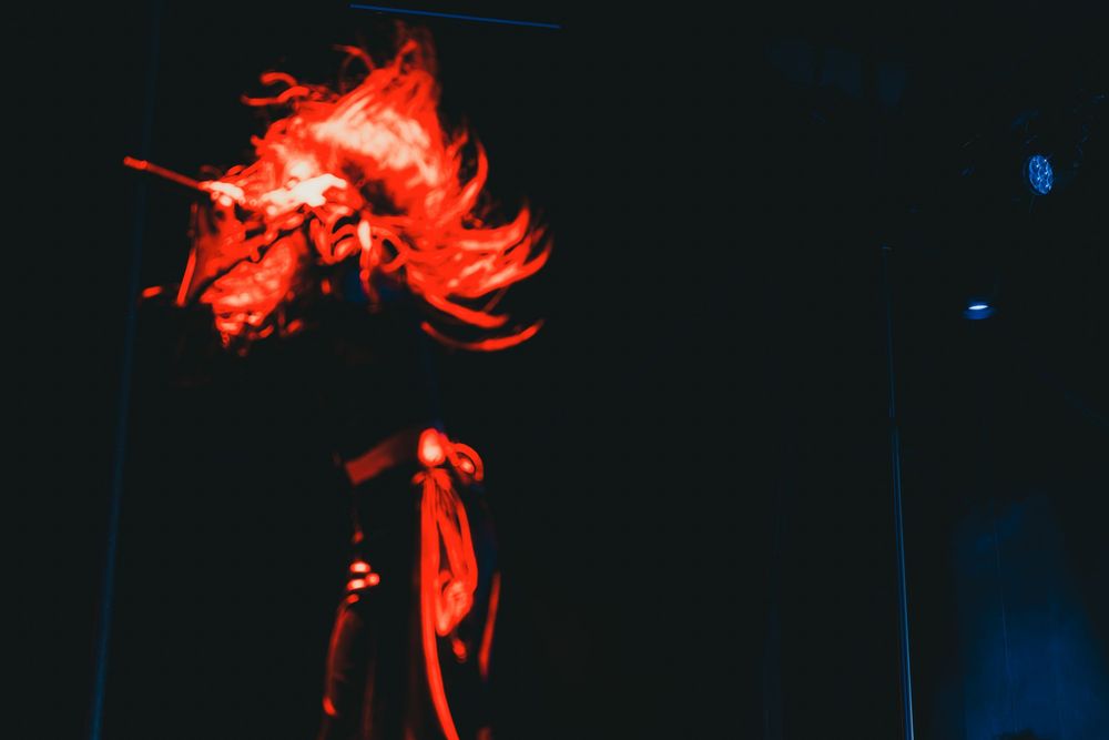 Dramatic silhouette of a performer on stage illuminated by bright red flames against a dark blue background.