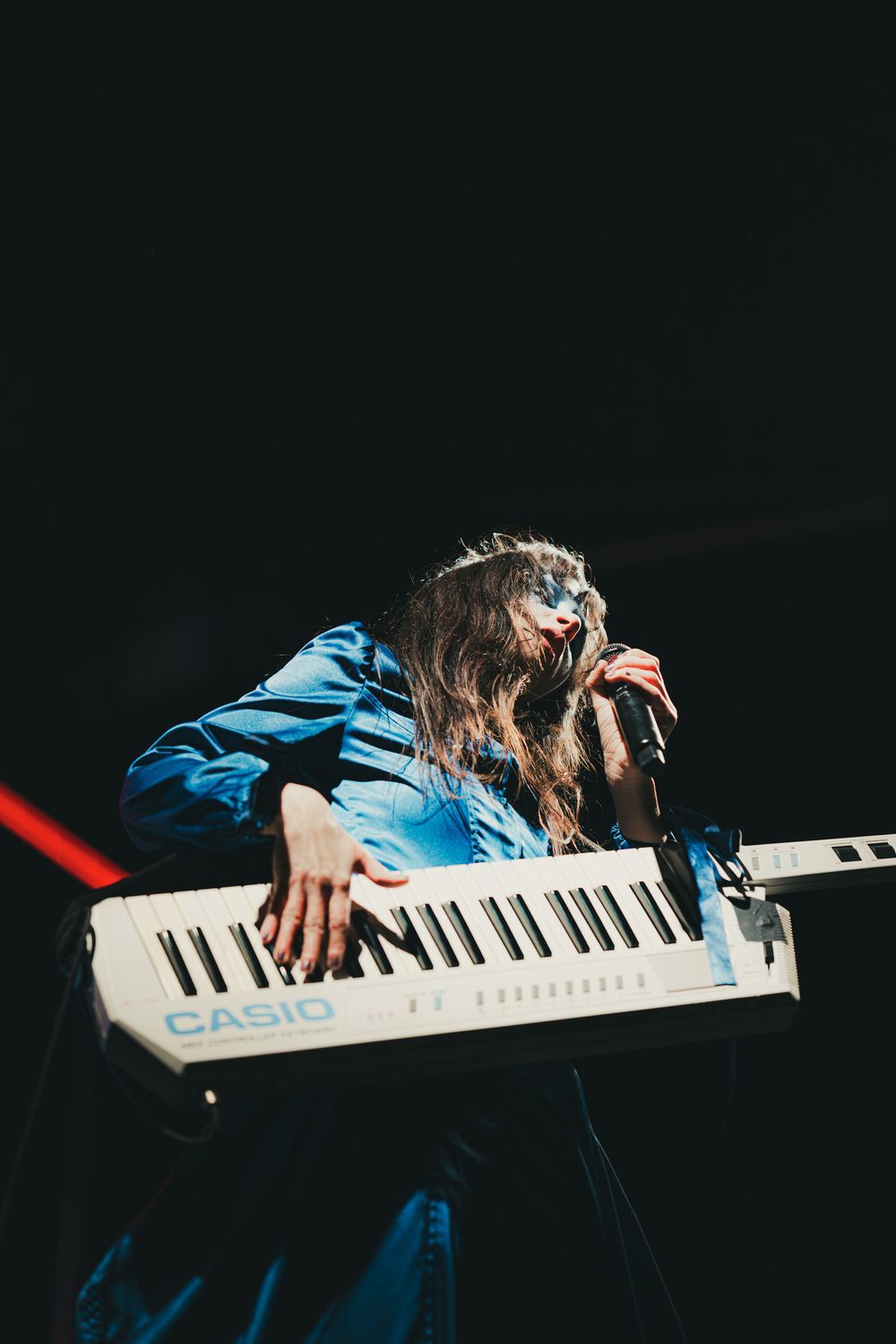 Hands playing a white Casio digital keyboard against a dark background with dramatic lighting.