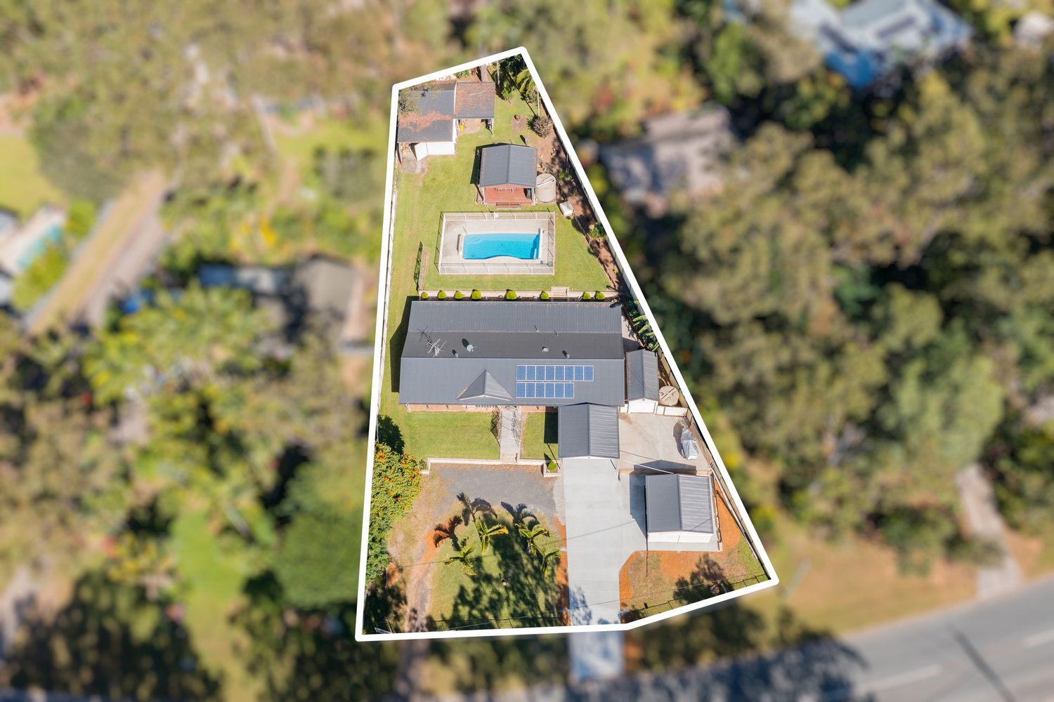 Aerial view of a triangular residential property with a pool, solar panels, and lush green surroundings.