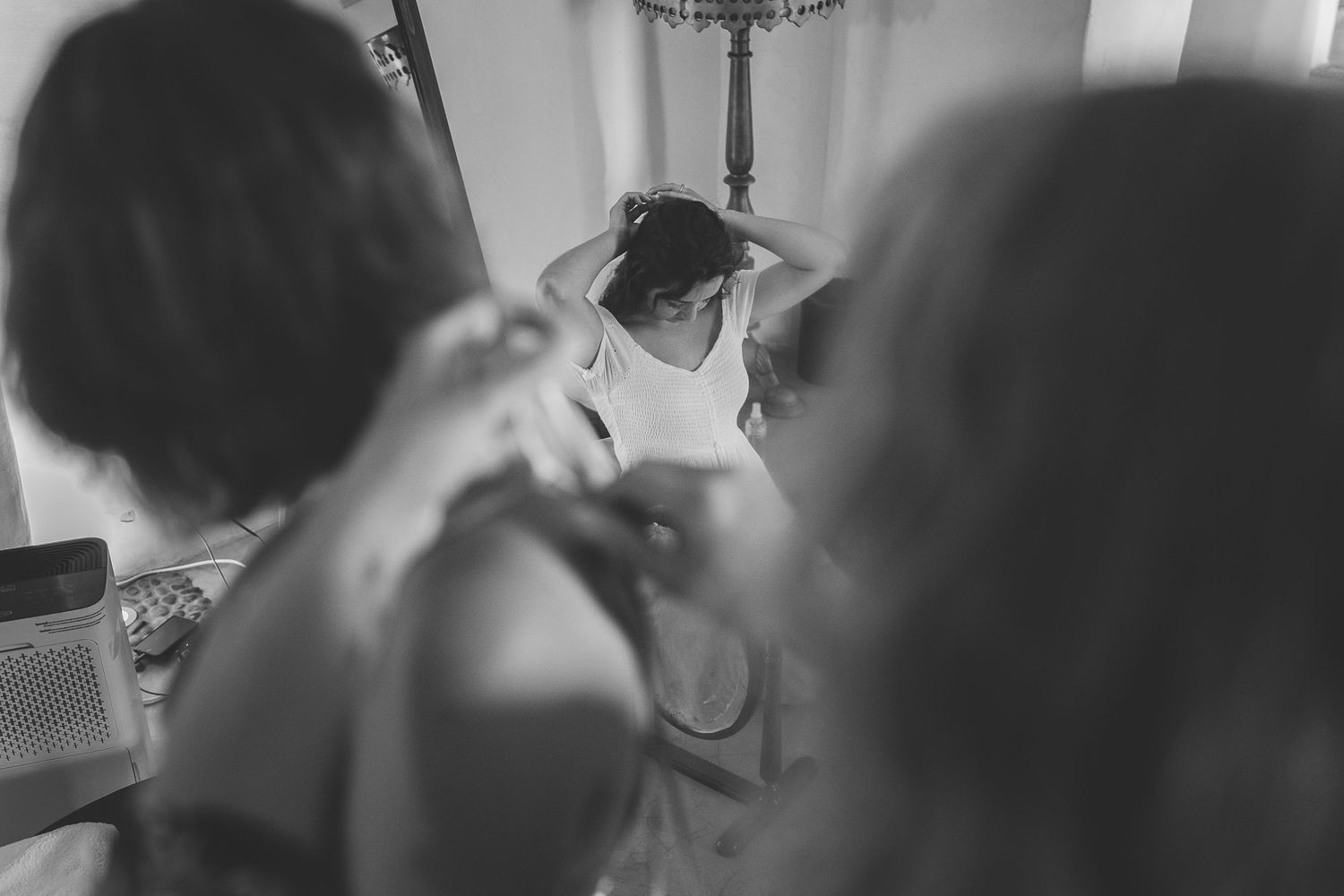 A Santorini bride gets ready for her dissemination wedding viewed through two of her party also getting ready.