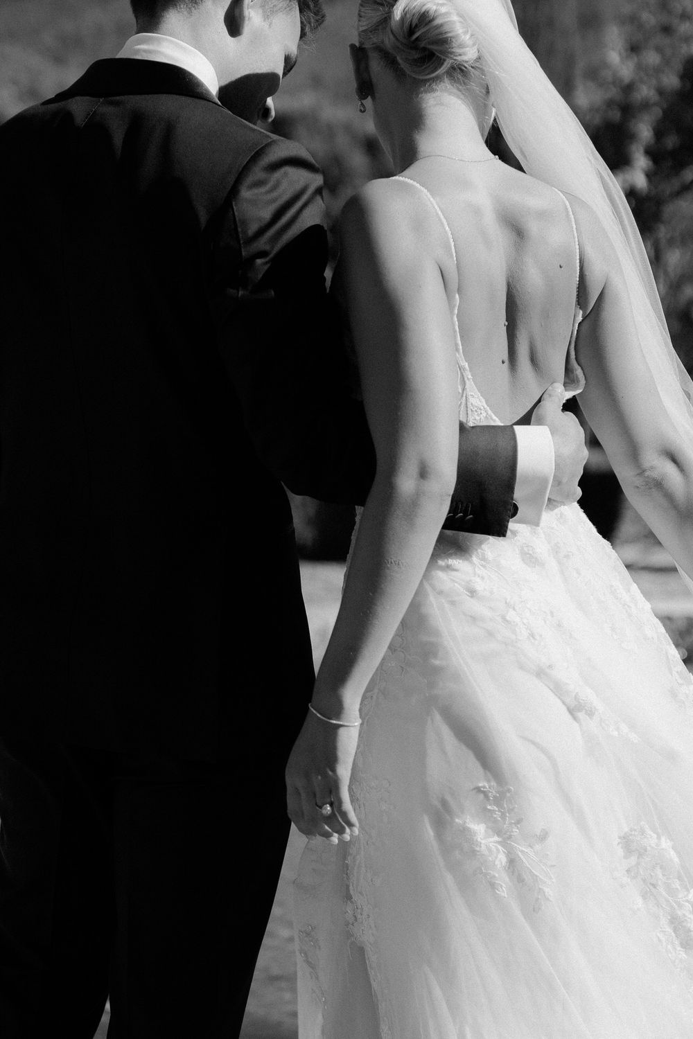 Black and white wedding photo showing a bride in a backless gown standing close to a groom in a dark suit.