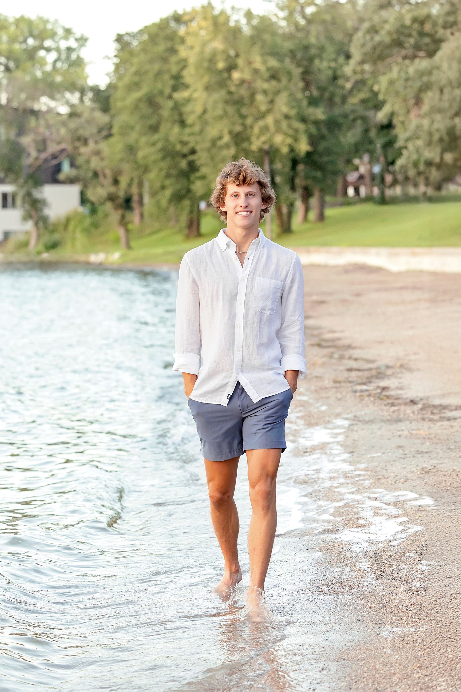 High school senior boy standing near shoreline during Clear Lake Iowa senior photos