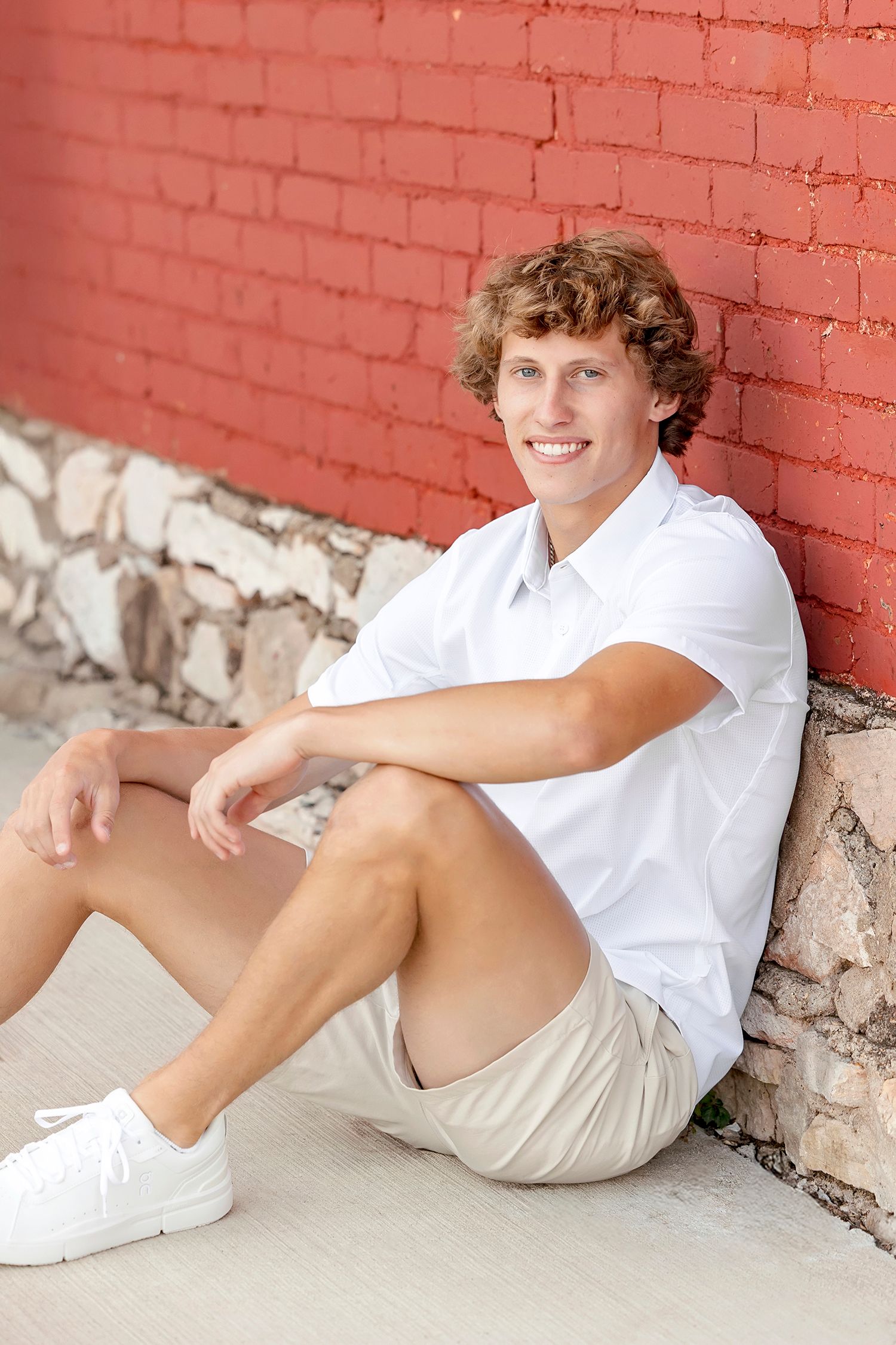 Senior boy sitting in front of red brick wall during Clear Lake Iowa senior photography session