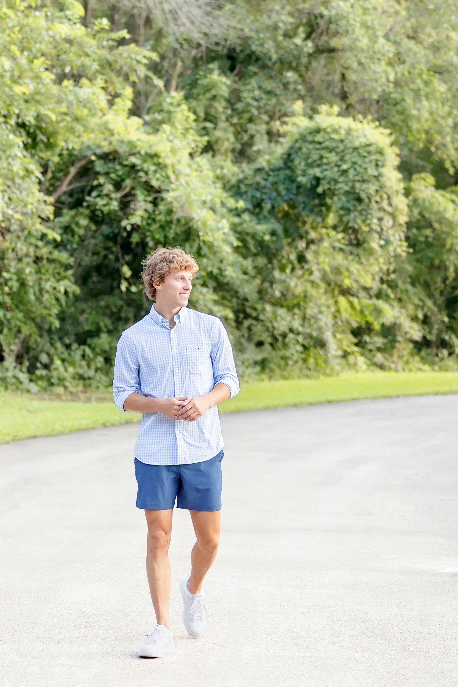 Senior boy walking down tree lined path during Clear Lake Iowa senior photo session at State Beach.