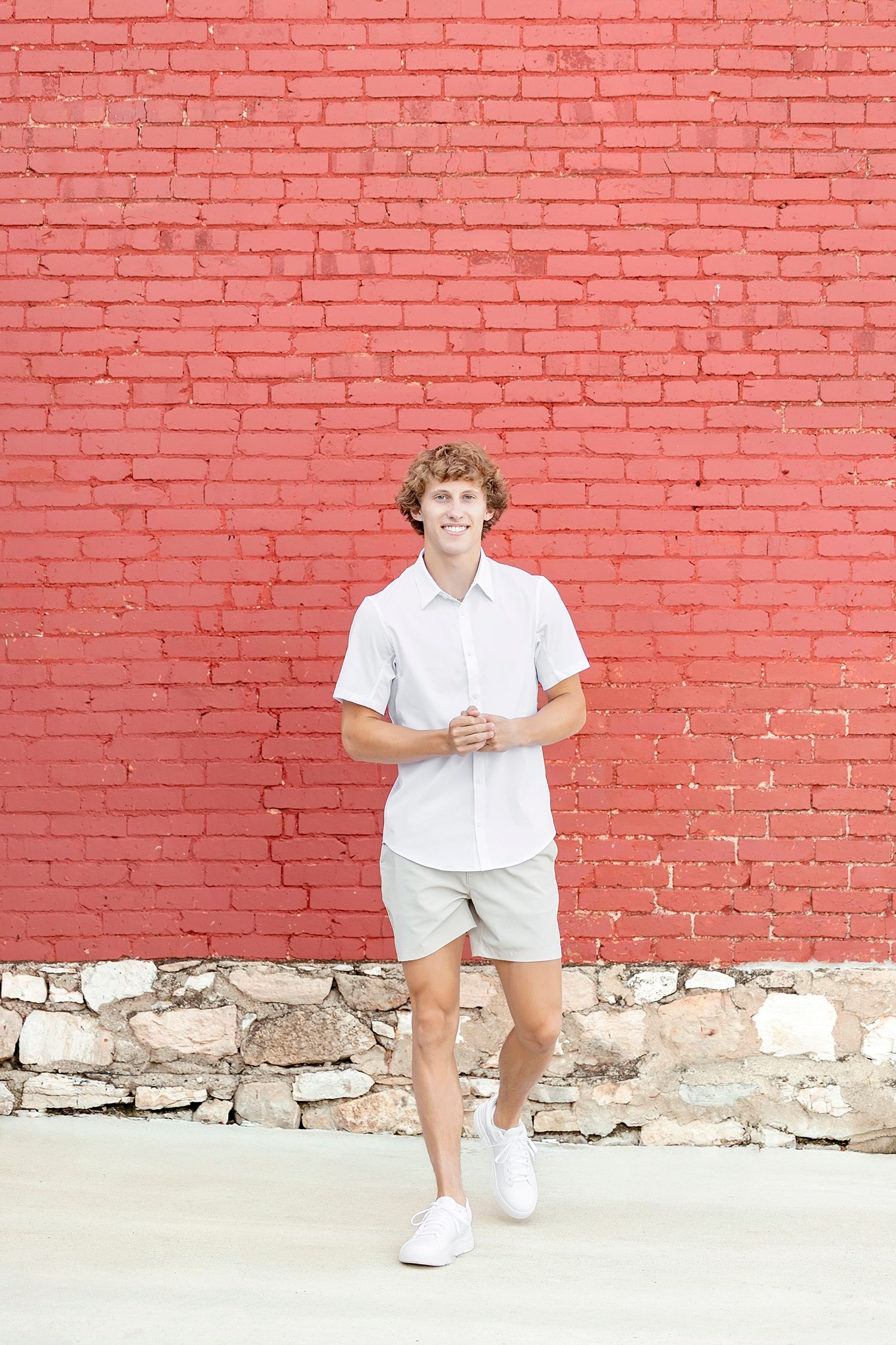 A sequence of casual poses against a bright red brick wall with white stone foundation.