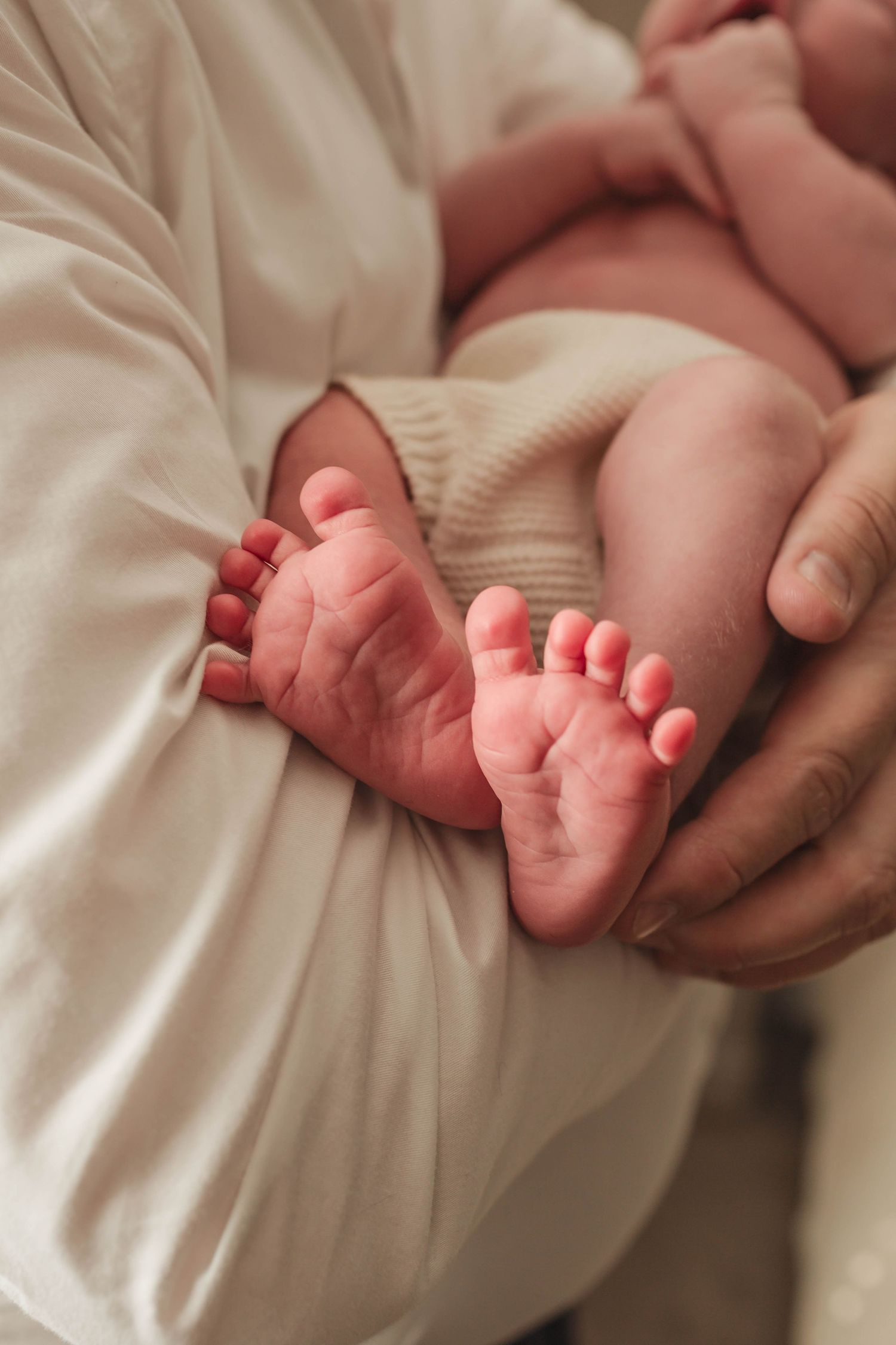 A series of close-up shots showing tiny newborn baby feet being gently cradled in adult hands against white fabric.