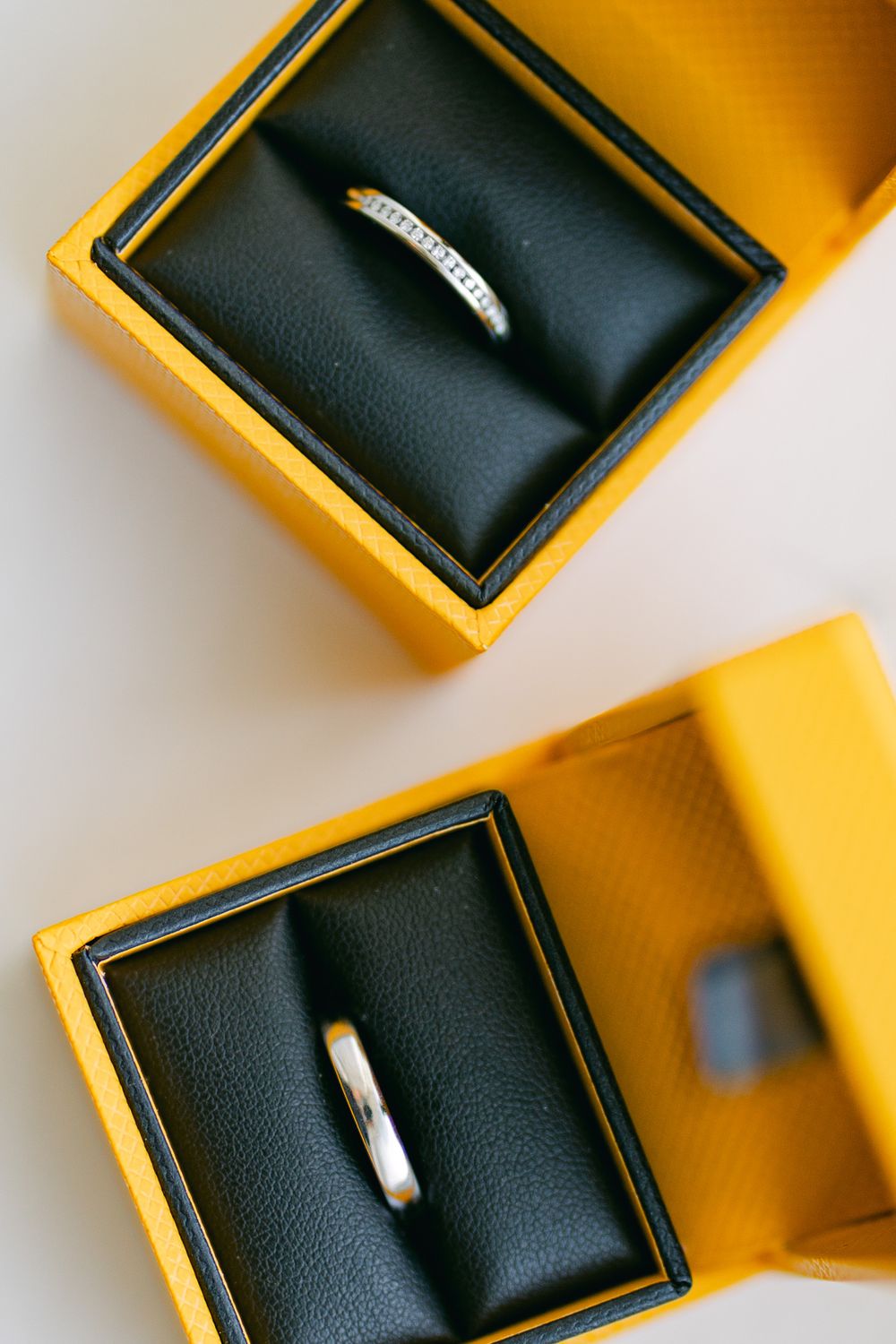 Black leather jewelry box with yellow edges sits open on white surface, displaying its elegant interior.