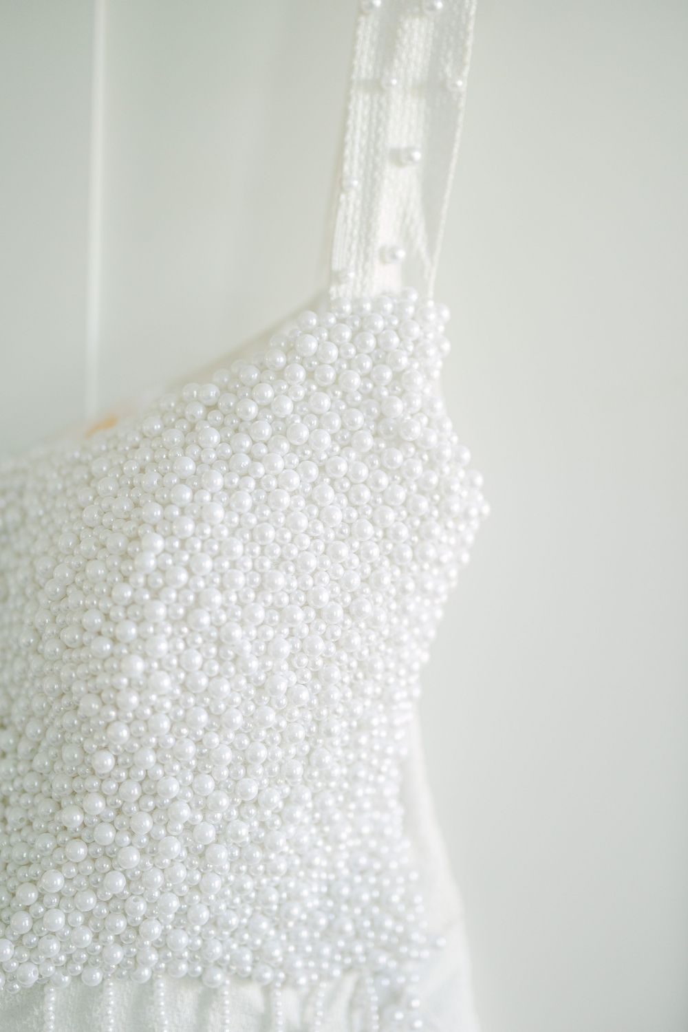 Close-up detail of a white wedding dress bodice adorned with delicate pearl embellishments.