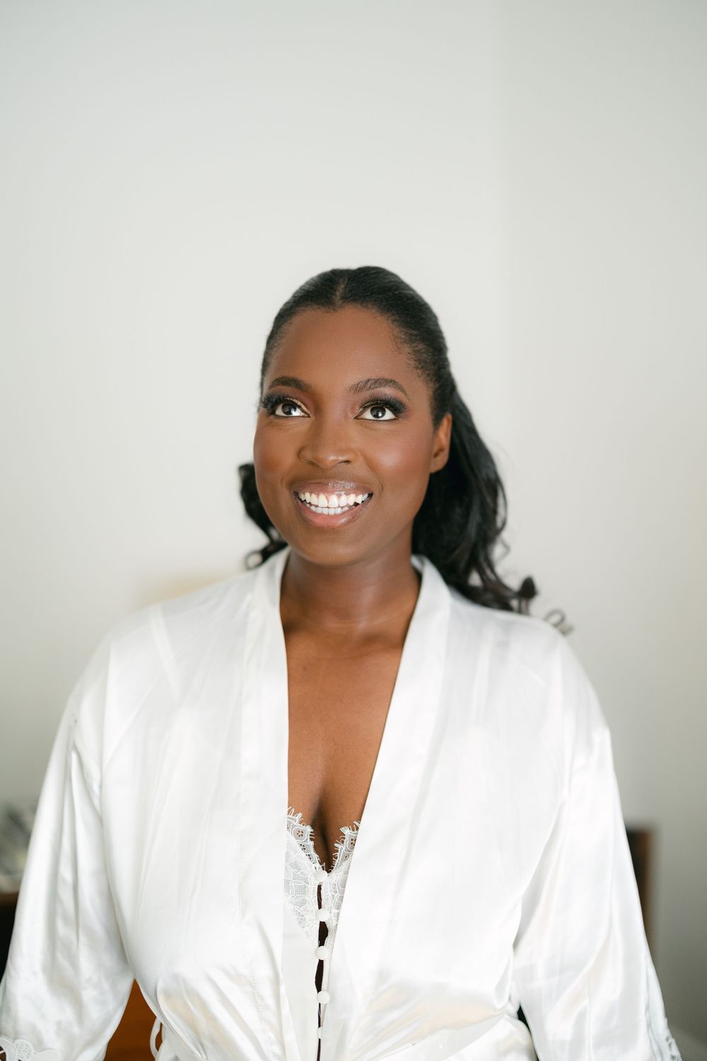 A portrait of someone wearing a white robe against a light background, with a bright smile and dark hair.