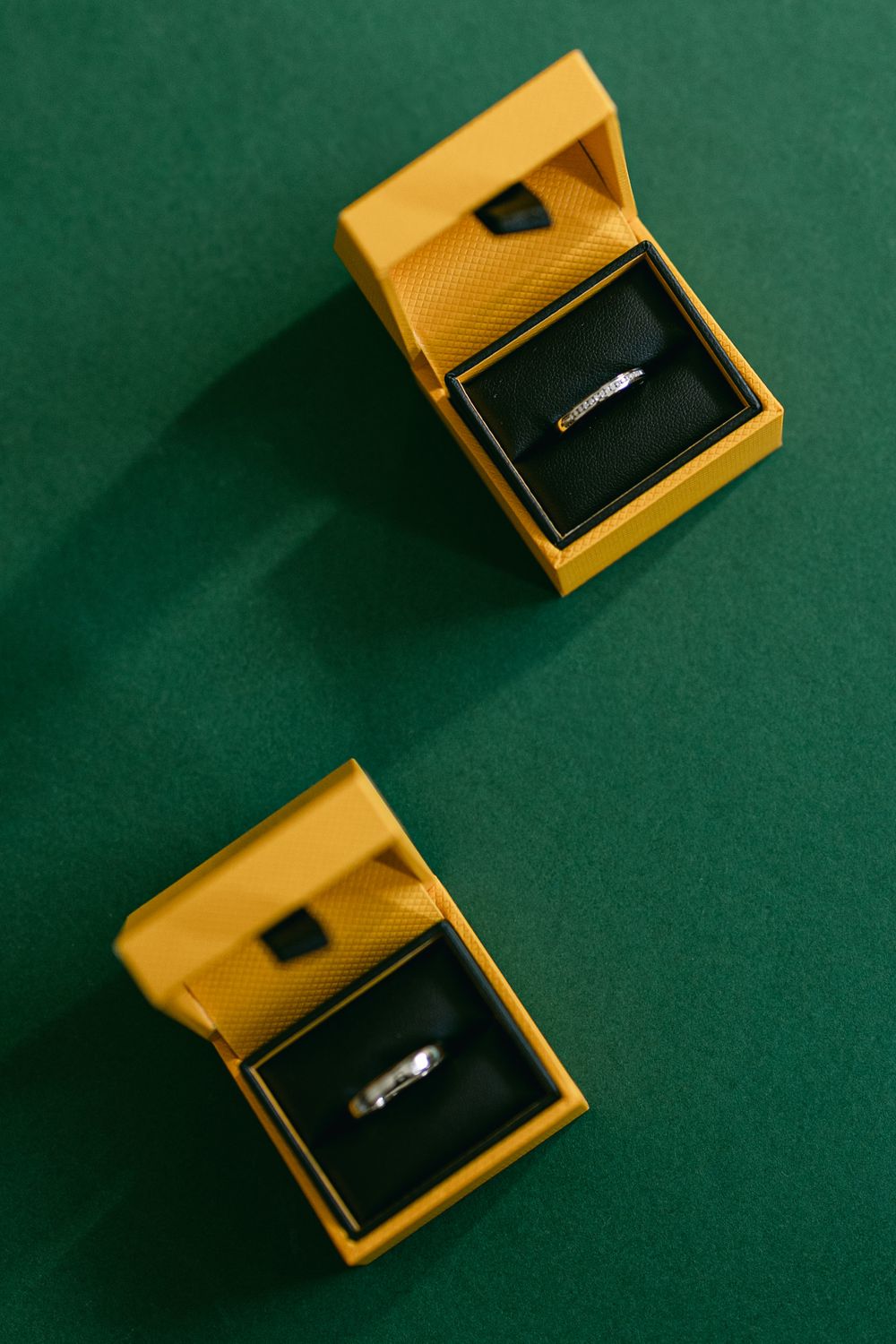 Yellow jewelry boxes with rings displayed on dark green velvet background.