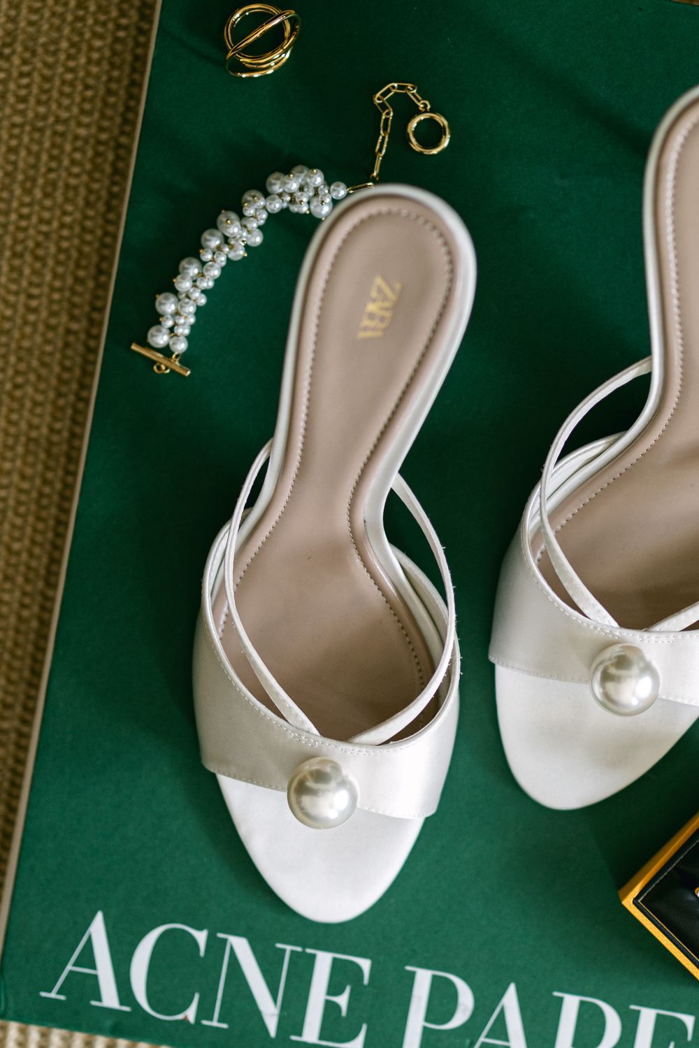 White bridal shoes with pearl embellishments displayed against a dark green background with elegant gold accents.