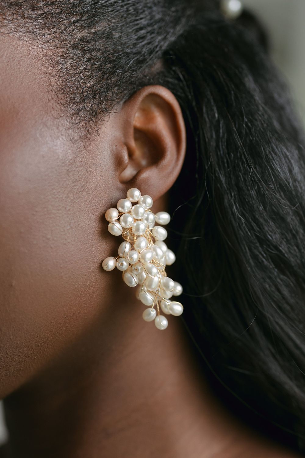 Close-up of a cluster pearl statement earring against dark hair and skin.