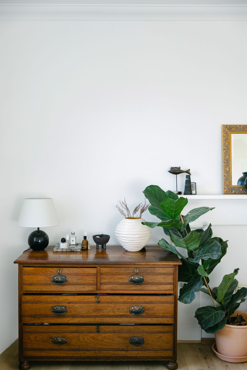 A wooden dresser styled with plants and decorative objects against a white wall in multiple angles.