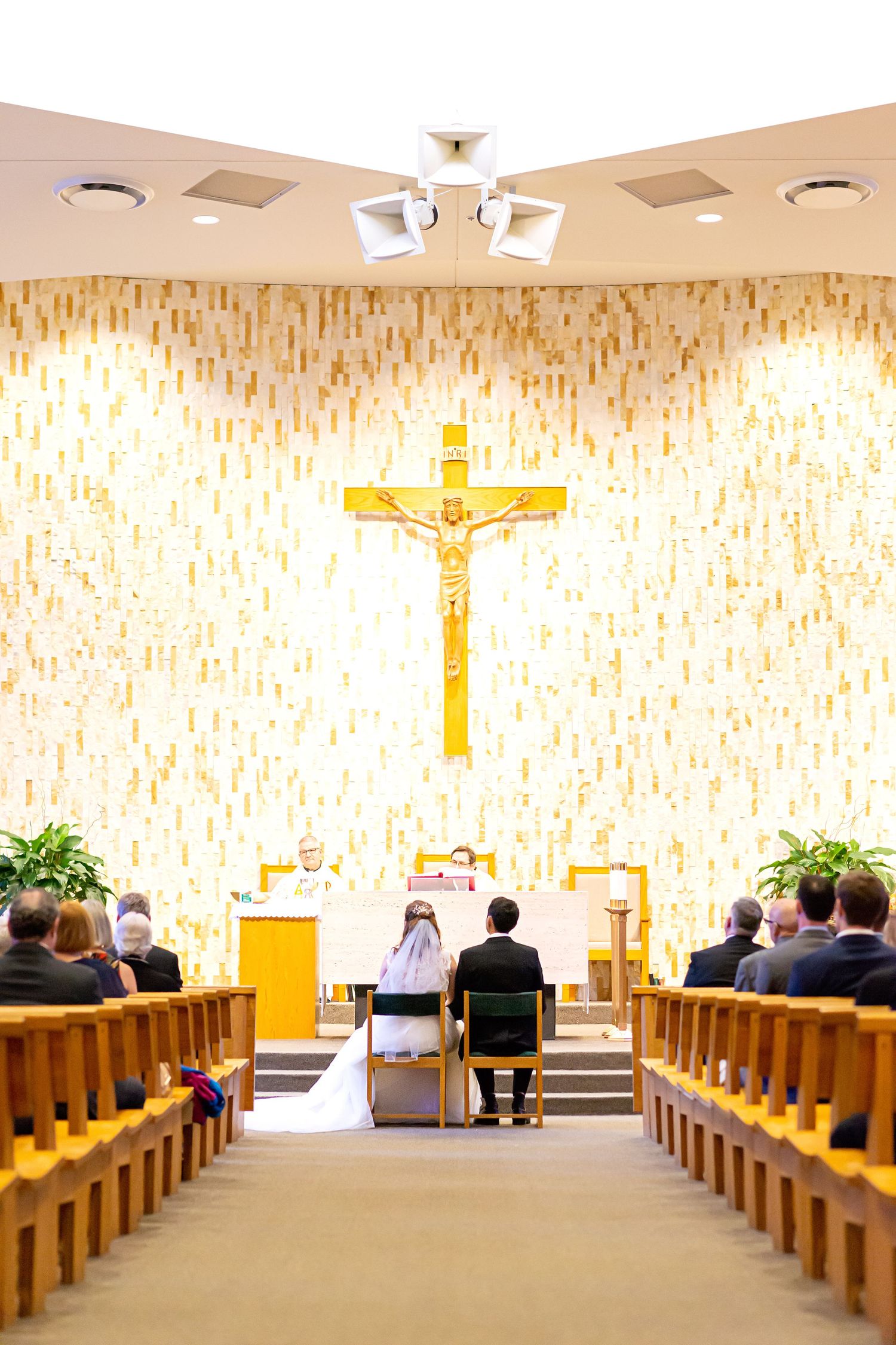 Modern church interior with wooden pews, beige patterned walls, and a golden crucifix at the altar.