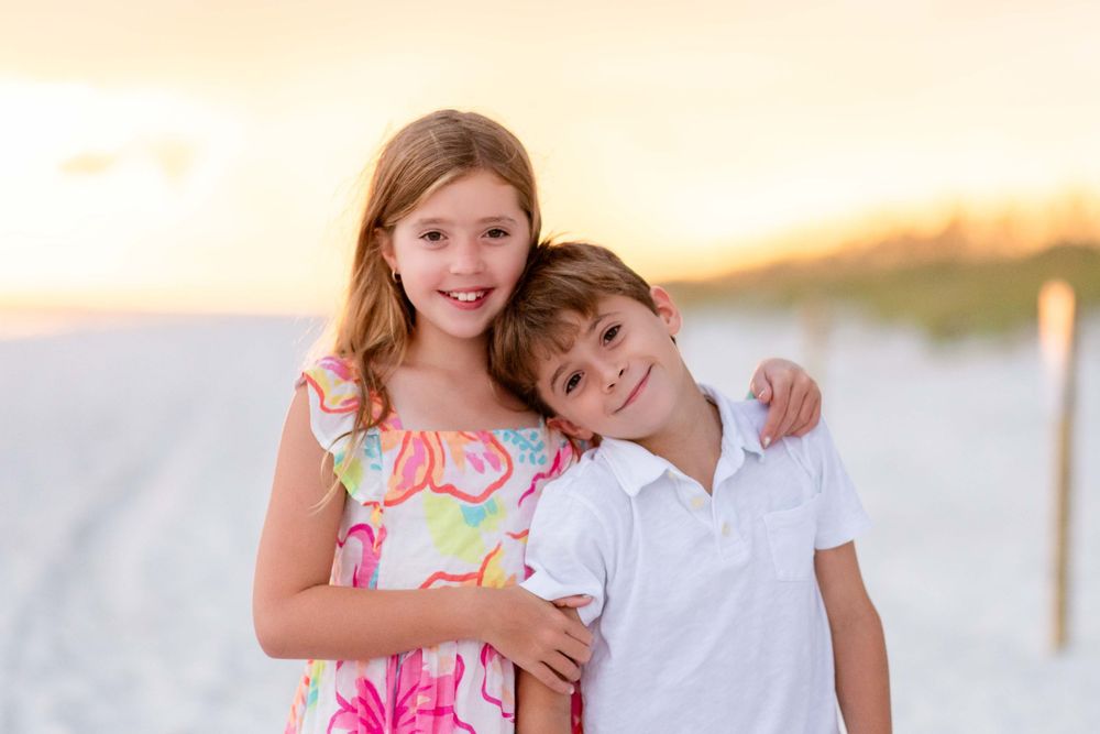 A series of family beach portraits at sunset with people wearing coordinated white and pink outfits.