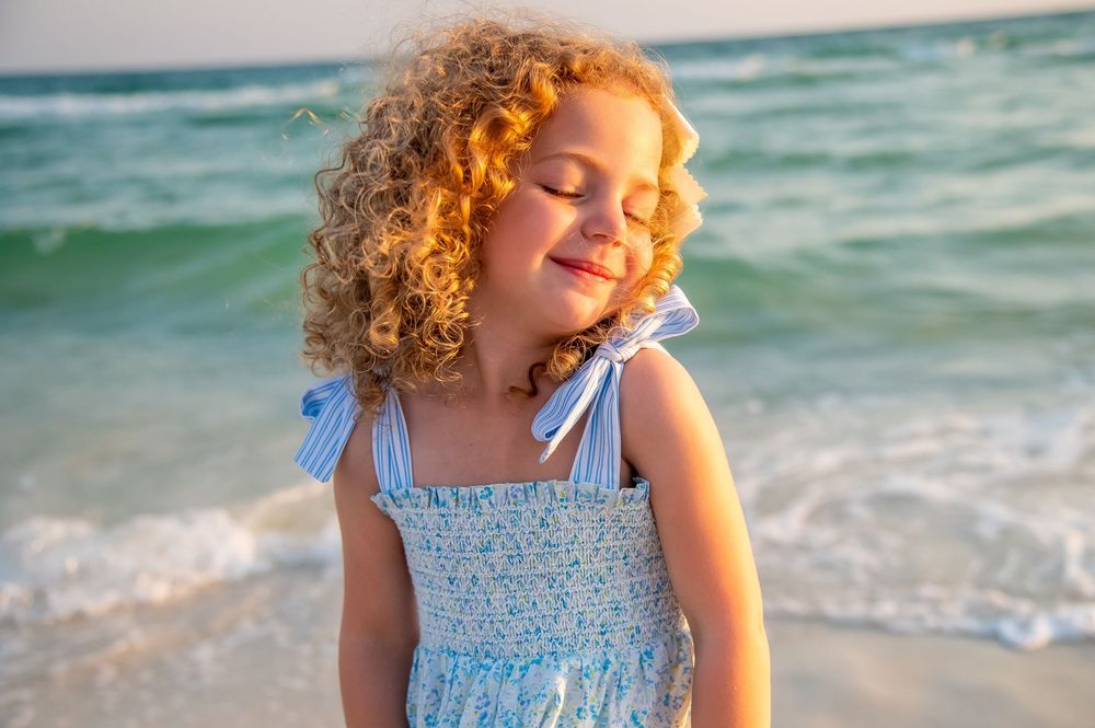 Young girl with curly hair playing joyfully at the beach during sunset.
